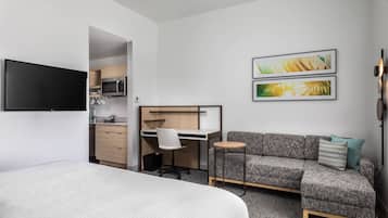 A modern hotel room with a bed, a sofa, a desk, and a television.
