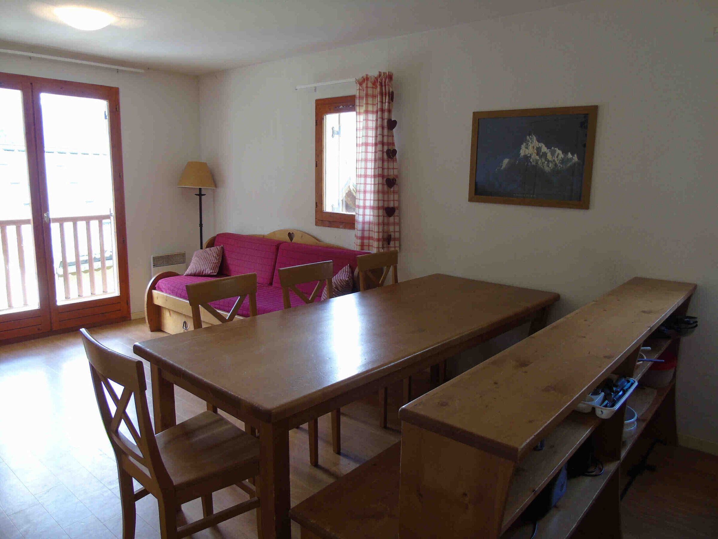 A dining area with a wooden table and chairs, a sofa, and a painting on the wall.