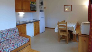 A compact kitchen with wooden cabinets, a microwave, a refrigerator, and a dining area with a table and chairs.