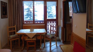 A dining area with a table and chairs, a window with a view of trees, a television on the wall, and a door leading to another room. - Cozy studio 4 ppl, near gondola & shops (Valfréjus)