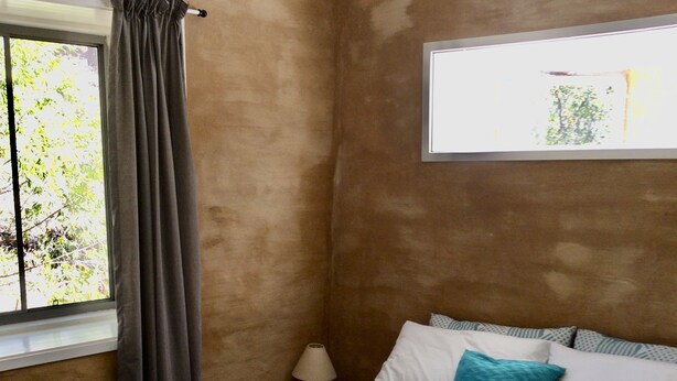 A bedroom with a bed, a nightstand, a lamp, a window with curtains, and a view of trees.