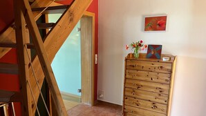 Una escalera de madera, un aparador de madera con cajones, una puerta y un cuadro colgado en la pared.
