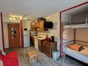 A compact room with a bunk bed, a kitchenette with wooden cabinets, a microwave, and a small table.