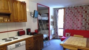 Une cuisine compacte équipée d’une cuisinière, d’un lave-vaisselle et de meubles de rangement en bois. On y trouve également un petit coin repas avec une table et des chaises.