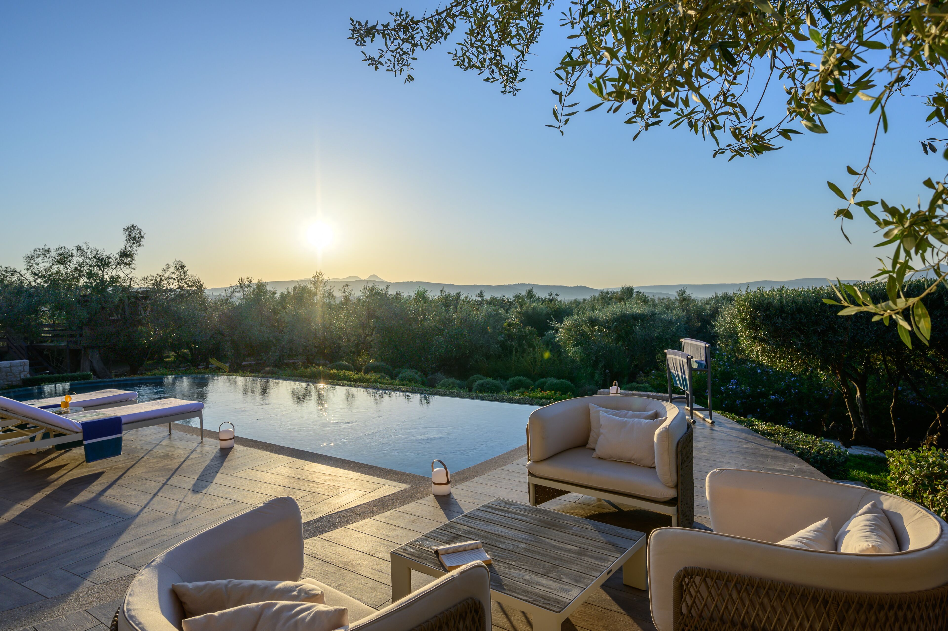 A serene outdoor setting with a pool, lounge chairs, and a wooden deck overlooking a lush landscape.