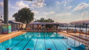 A swimming pool with lanes marked by numbers, a covered seating area, and a view of a body of water. - Jewel Maadi Cabins and Club (Cairo)