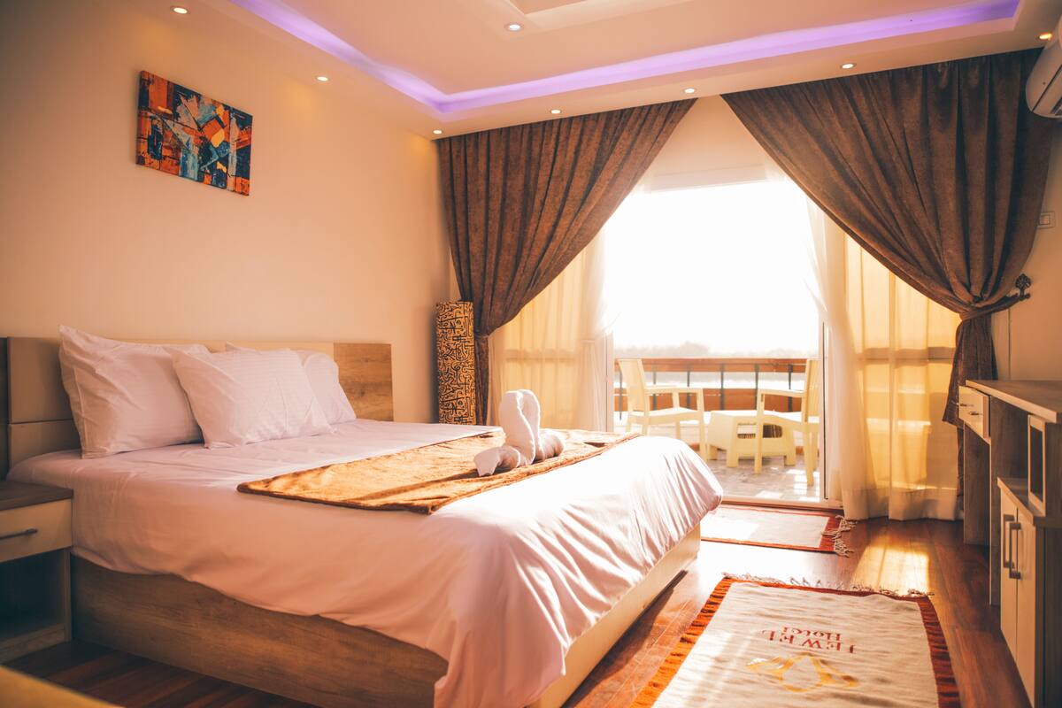 Une chambre d’hôtel avec un lit, une table de chevet, un bureau, une chaise et un balcon donnant sur une vue agréable.