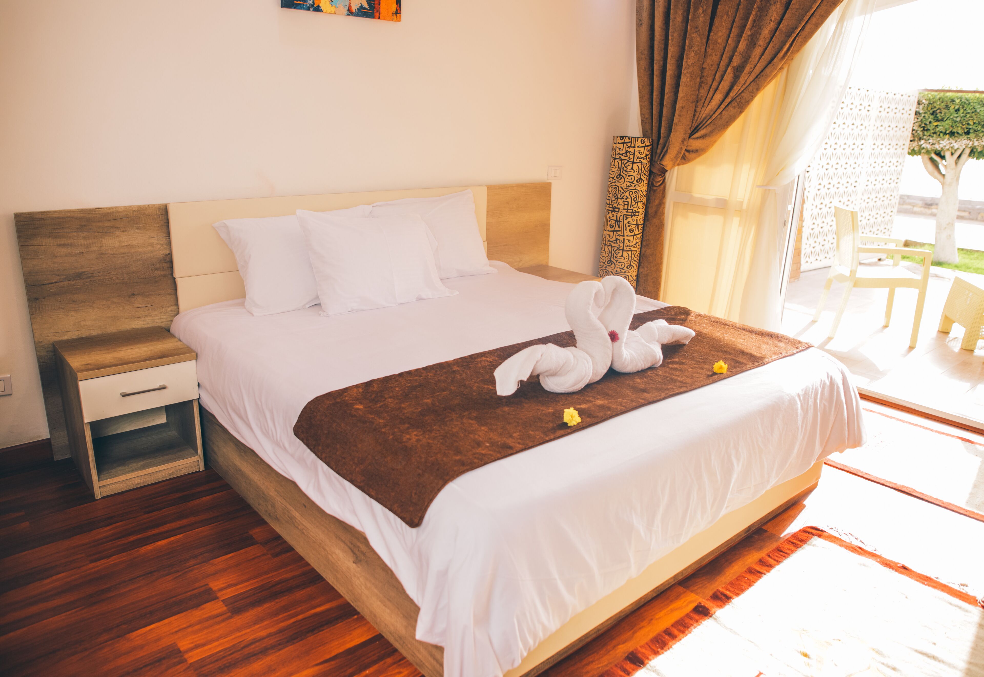 Una cama bien hecha con sábanas blancas, cabecera de madera y manta marrón.