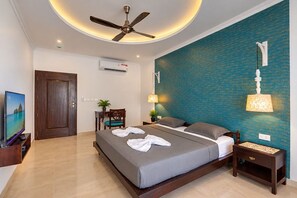 A hotel room with a bed, a ceiling fan, a TV, a desk, and a wall-mounted lamp. - Stay at a Luxurious 14 Bedroom Villa in Calangute with Pool, Jacuzzi, Mini Golf (Calangute)