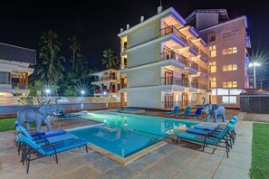 A multi-story hotel with a swimming pool, lounge chairs, and decorative elephant statues.