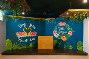 A reception area with a blue wall featuring a swan and heart design, a wooden reception desk, and tropical plant decorations.
