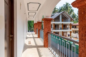 A corridor with a balcony overlooking a pool and a building with a balcony.