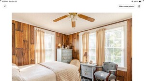 A bedroom with a wooden paneled wall, a bed with a quilted cover, a nightstand with a lamp, and a chair. - Cozy confortable (Pulaski)