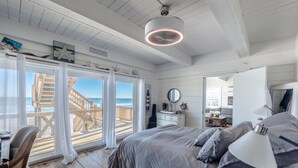 A bedroom with a large bed, a desk, and a view of the beach through a sliding glass door. - Vintage Vacation Pet Friendly, Ocean Views! (Surf City)