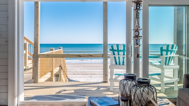 A beach view from a room with a large window, wooden deck, and two beach chairs. - Vintage Vacation Pet Friendly, Ocean Views! (Surf City)