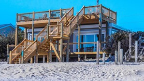 A beachfront property with a wooden staircase leading to a balcony, a large window, and a statue. - Vintage Vacation Pet Friendly, Ocean Views! (Surf City)
