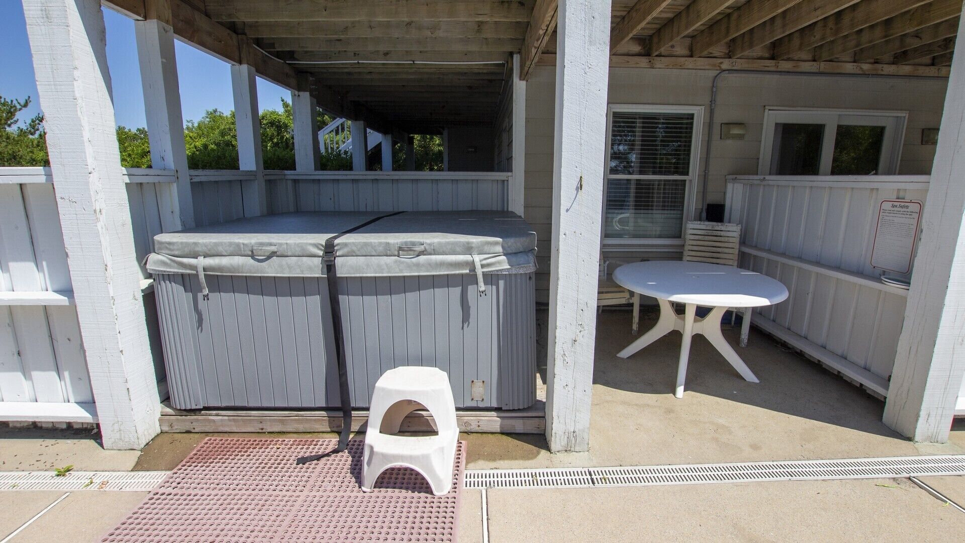 A covered outdoor area with a hot tub, a small table, and a pet potty.