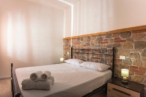 Een bed met een houten hoofdbord, twee bedlampen en een keurig opgevouwen handdoek op het bed.