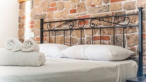 Un letto con lenzuola bianche, una parete in pietra e una testiera in metallo.