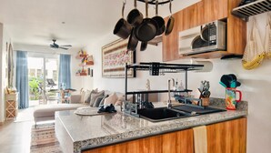 A modern kitchen with a central island, a hanging pot rack, and a microwave above the stove. - Private Tropical Home  with Pool (Akumal)