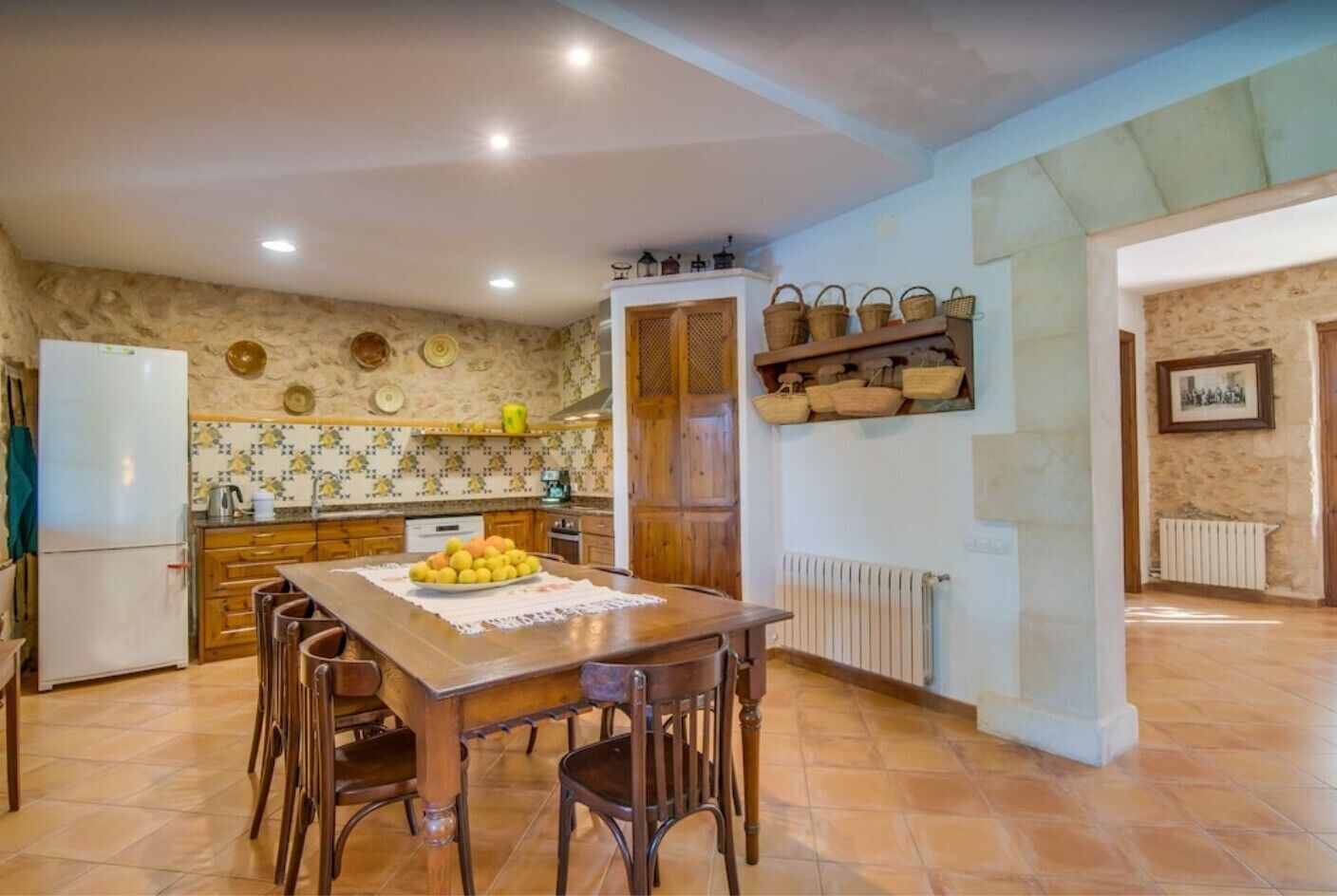 A kitchen with a dining table, chairs, a refrigerator, and a wall with shelves.