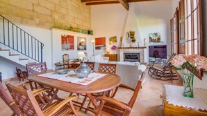 A dining area with a wooden table and chairs, a fireplace, and a staircase. - Beautiful Country Home “Son Vanrell” with Mountain View, Pool, Wi-Fi, A/C, Terrace & Garden; (Campos)