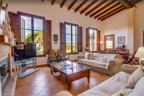 A living room with a fireplace, wooden beams, a television, and a dining area with chairs and a table.