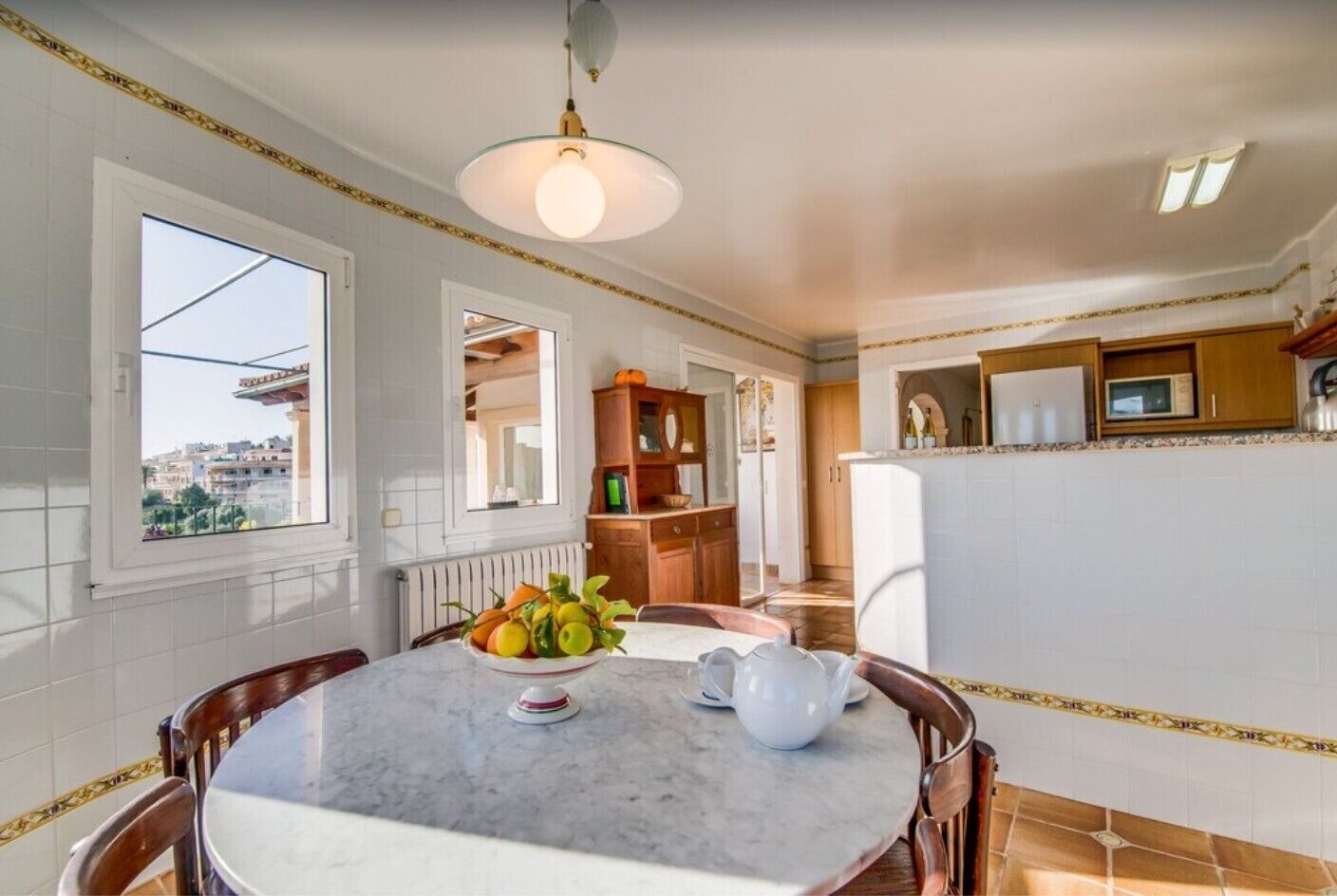 Un comedor con una mesa de mármol, un cuenco de fruta y una jarrón. Se ve una ventana con vistas a edificios.