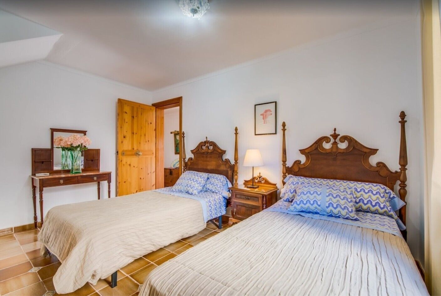 Une chambre avec deux lits, une armoire en bois, une table de chevet, un miroir et une porte.
