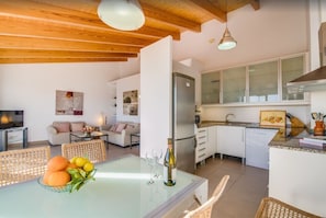 Eine moderne Küche mit weißen Schränken, einem eingebauten Backofen und einer Essecke mit Glastisch und Korbstühlen.
