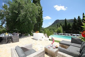 En uteplats med möbler av rotting, en pool och en bergig bakgrund.