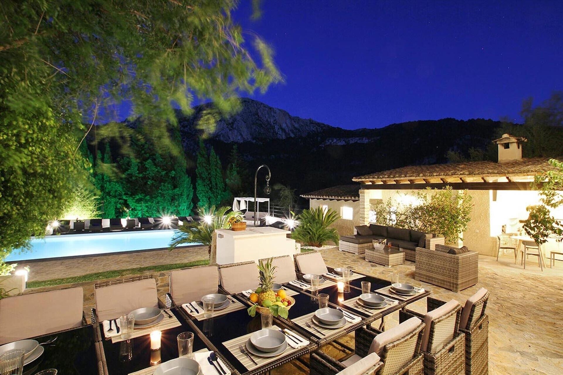 An outdoor dining area with tables set for two, a pool, and a mountain backdrop.