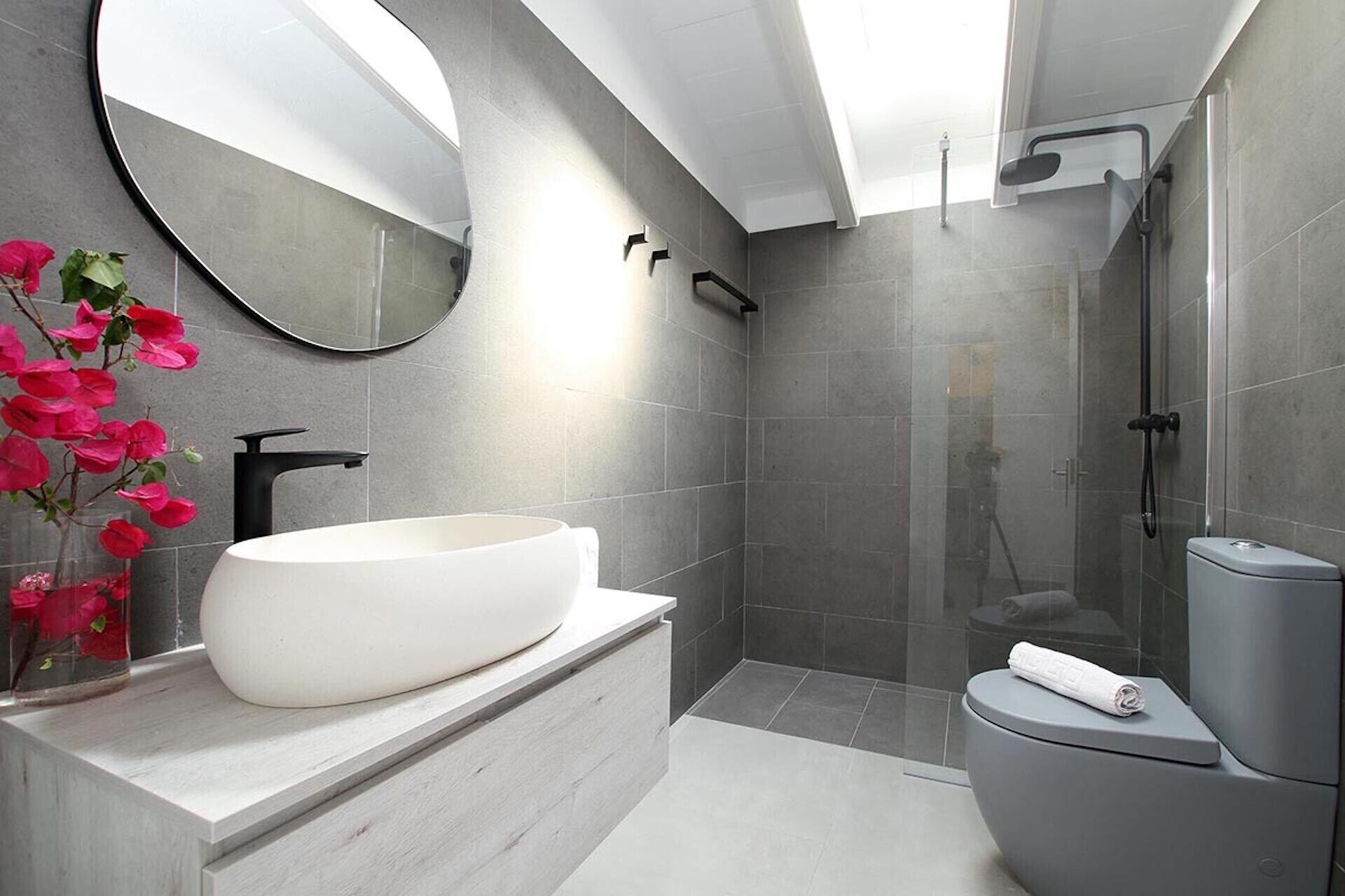A modern bathroom with a large round sink, a toilet, and a shower area.