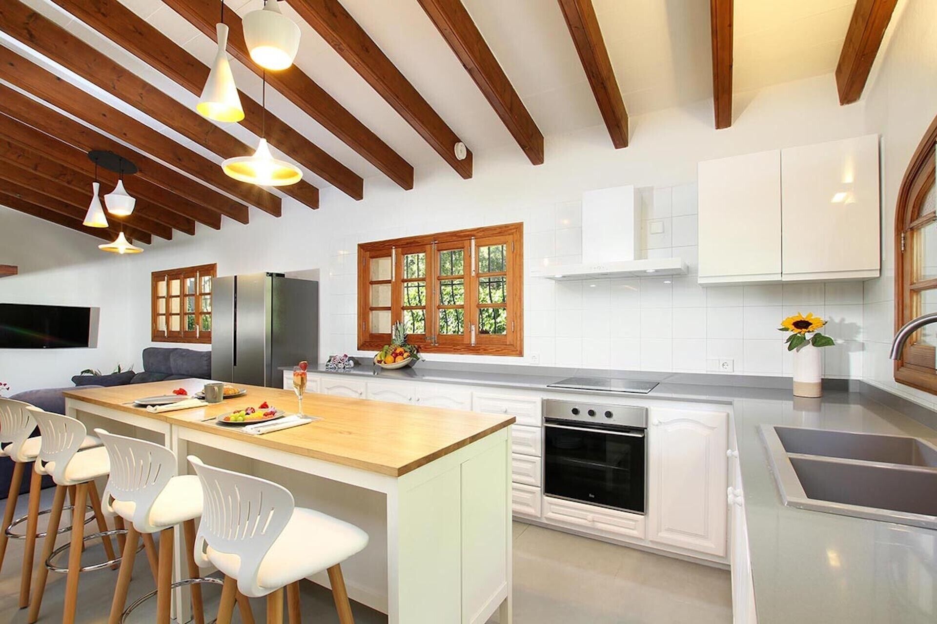 A modern kitchen with white cabinets, a wooden ceiling, and a large island with bar stools.