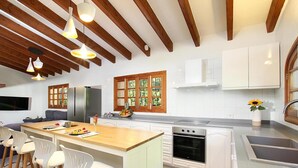 A modern kitchen with white cabinets, a wooden ceiling, and a large island with bar stools. - Finca “Jaume Romona” with Mountain View, Pool, Wi-Fi, Air Conditioning, Terrace & Garden (Pollensa)