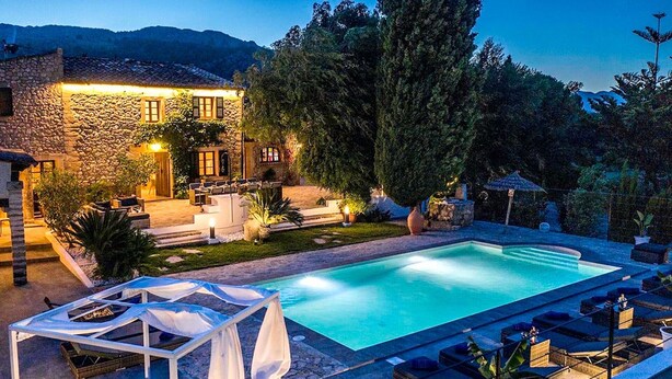A swimming pool with lounge chairs, a covered seating area, and a stone building with outdoor lighting. - Finca “Jaume Romona” with Mountain View, Pool, Wi-Fi, Air Conditioning, Terrace & Garden (Pollensa)