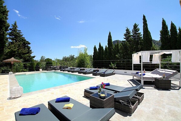 Et tagområde med swimmingpool, liggestole, et lille bord med en drink og en pergola.
