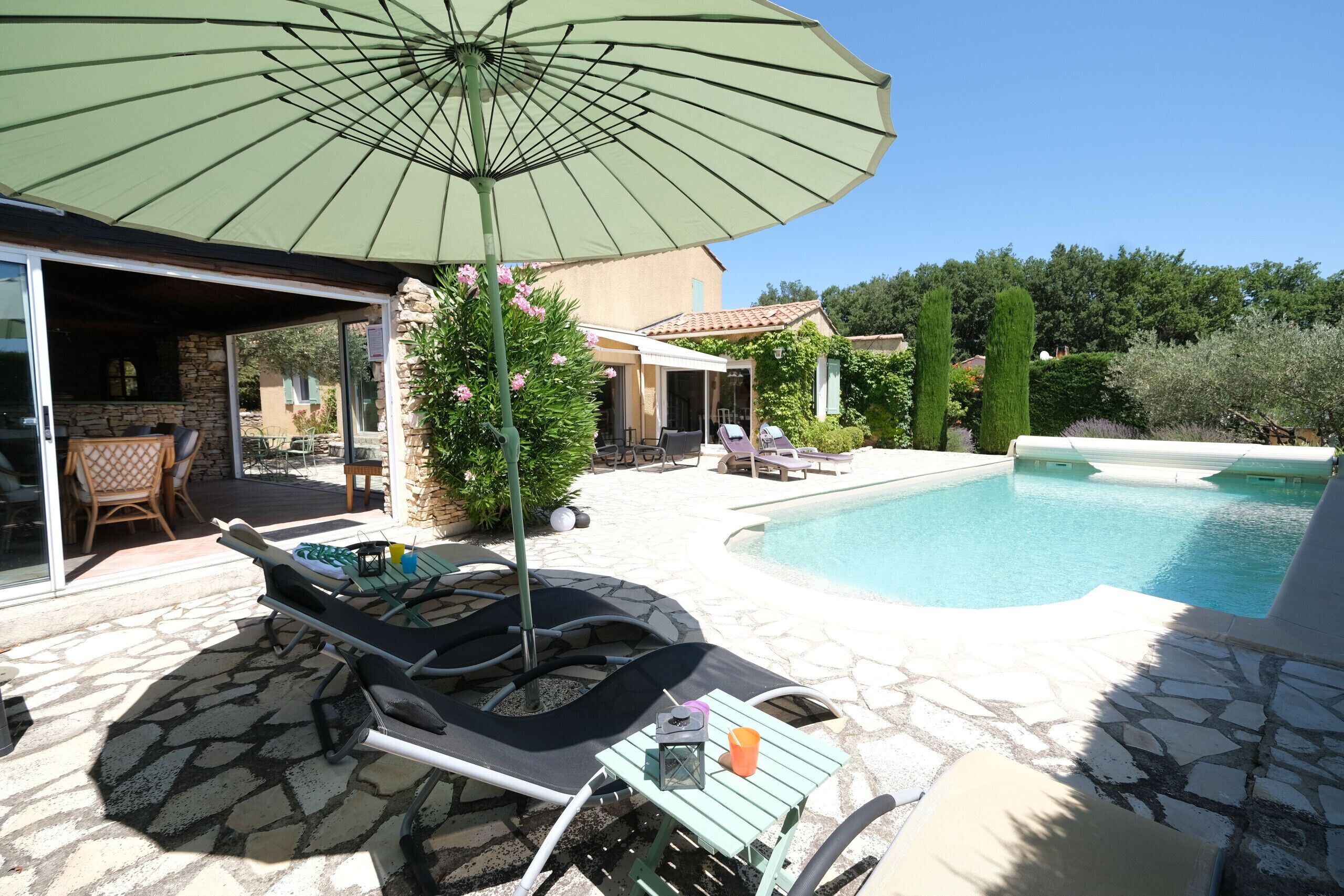 Un espace piscine extérieur avec des chaises longues, une table agrémentée d’une lanterne et un parasol.
