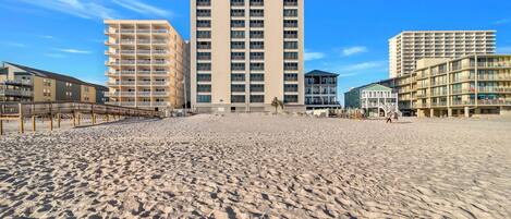 Una playa con un edificio alto en el centro, un paseo marítimo de madera a la izquierda y un edificio más pequeño a la derecha.