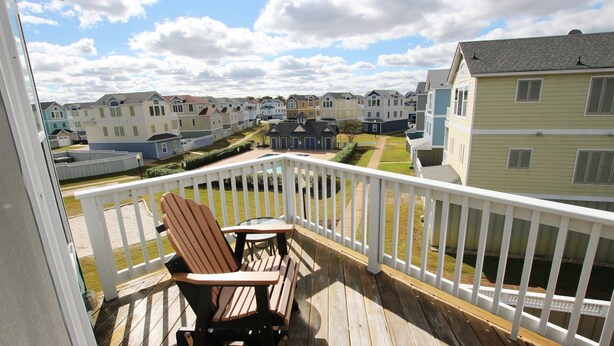 Una terraza de madera con una sola silla Adirondack, con vista a una hilera de casas coloridas bajo un cielo despejado.