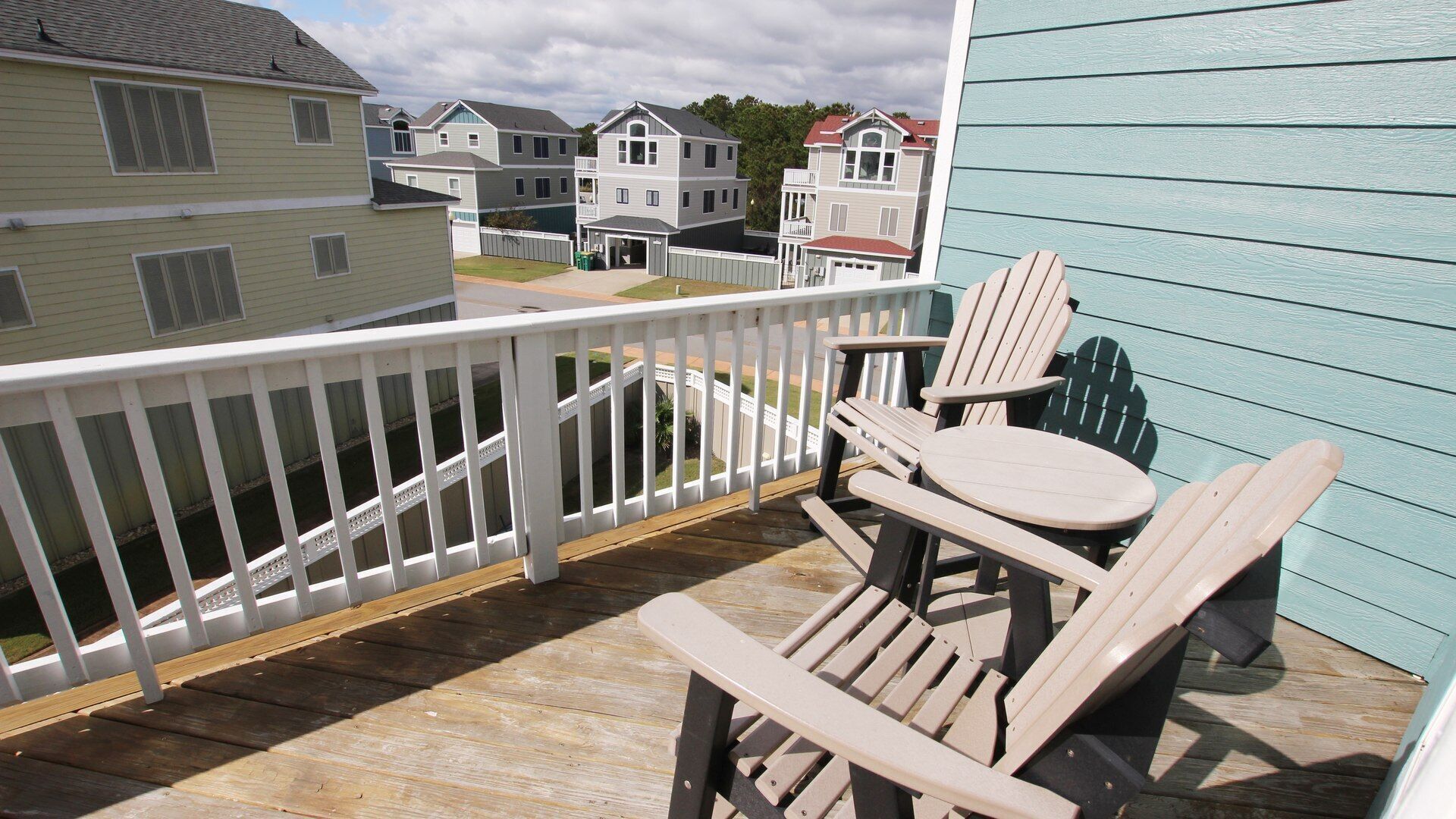 Een houten terras met een witte balustrade, twee Adirondack-stoelen en uitzicht op omliggende huizen.