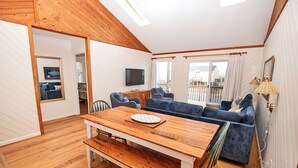 A cozy living room with a wooden dining table, blue sofa, and a TV mounted on the wall. - Semi-Oceanfront, 100 ft to beach access, Sun Decks, KH141, Blue Heaven (Kitty Hawk)