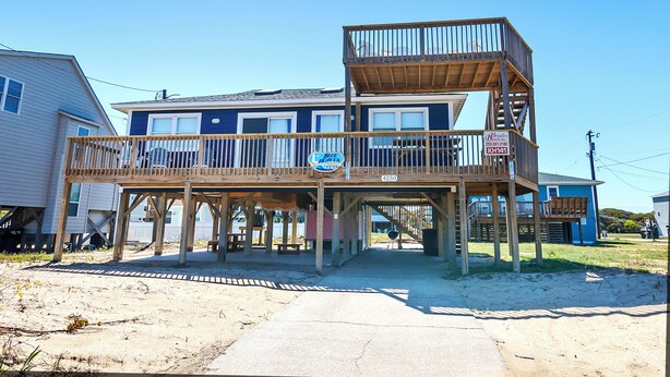A two-story wooden structure with a balcony, a sign indicating a business, and a clear sky. - Semi-Oceanfront, 100 ft to beach access, Sun Decks, KH141, Blue Heaven (Kitty Hawk)