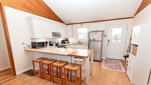 A modern kitchen with white cabinets, a wooden island with bar stools, a stainless steel refrigerator, and a window providing natural light. - Semi-Oceanfront, 100 ft to beach access, Sun Decks, KH141, Blue Heaven (Kitty Hawk)