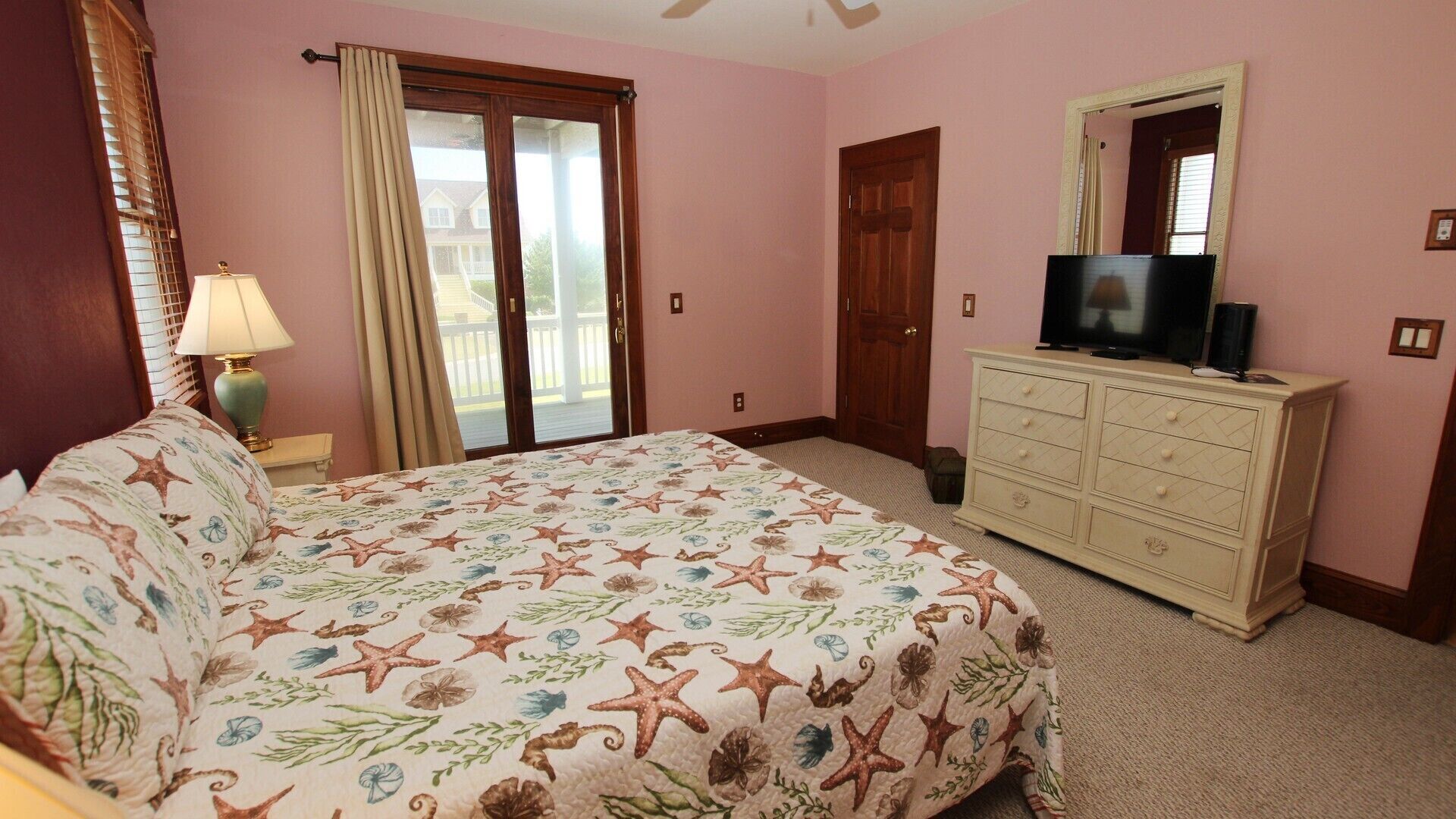 A bedroom with a bed, a dresser, a television, and a sliding glass door.