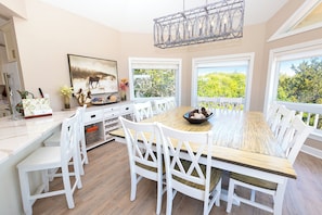 Un coin repas avec une table en bois, des chaises blanches, un lustre et un tableau au mur.