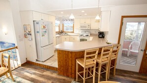 A modern kitchen with white cabinets, a central island with bar stools, a refrigerator, a microwave, and a stove. - Oceanside, Dogs Welcome, Private Pool, Hot Tub, Close to Beach Access, OL626, Celtic Dunes (Corolla)