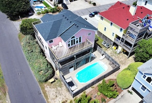 Una casa de dos pisos con piscina, terraza cubierta y jardín cercado.