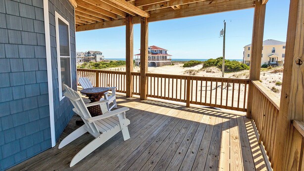 Une terrasse en bois offrant une vue sur la plage et les maisons en arrière-plan.