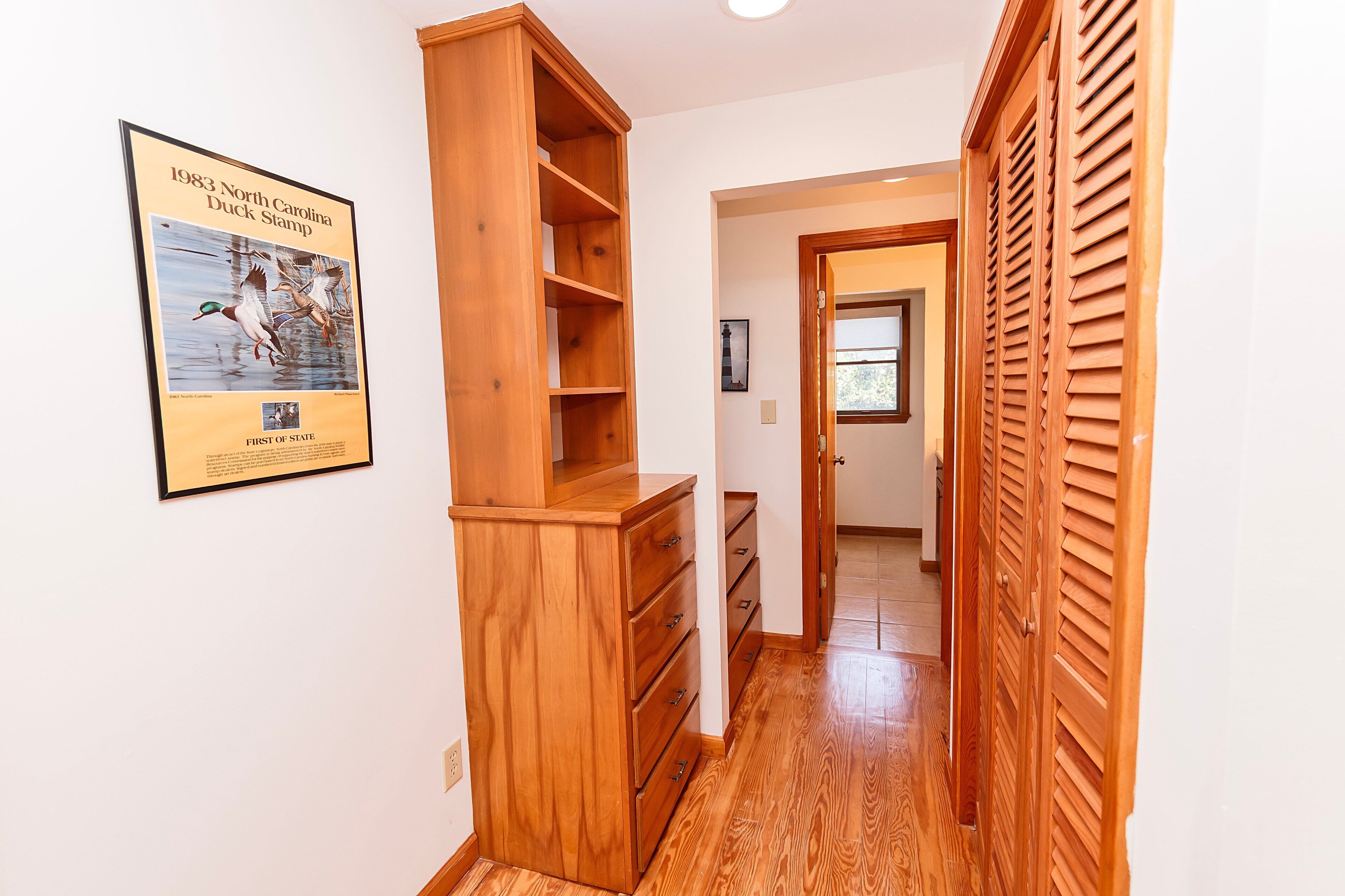 A hallway with wooden cabinets, a framed duck stamp, and a door with louvered shutters.